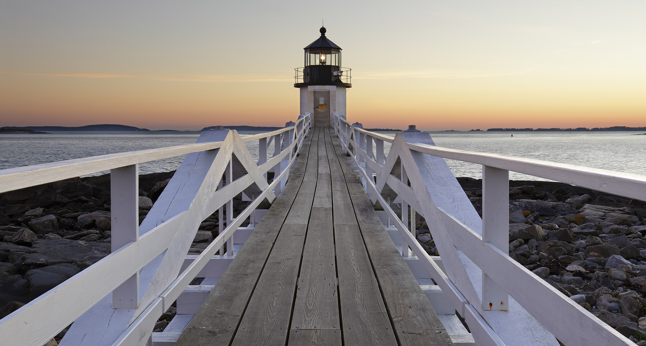 A quiet waterfront walkway and lighthouse at sunset